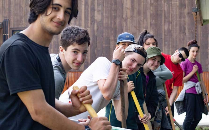 a group of outward bound students stop shoveling to smile at the camera during a service project